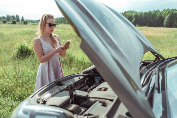 woman calls, writes reads message, in summer road, car broke down, an open hood, an accident, an emergency call, tow truck in the country. Pink dress sunglasses. stock photo