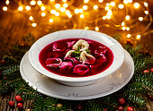 Christmas beetroot soup, red borscht with small dumplings with mushroom filling in a ceramic white plate on a wooden table