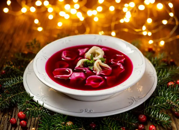 Christmas beetroot soup, red borscht with small dumplings with mushroom filling in a ceramic white plate on a wooden table .Traditional Christmas eve dish in Poland.