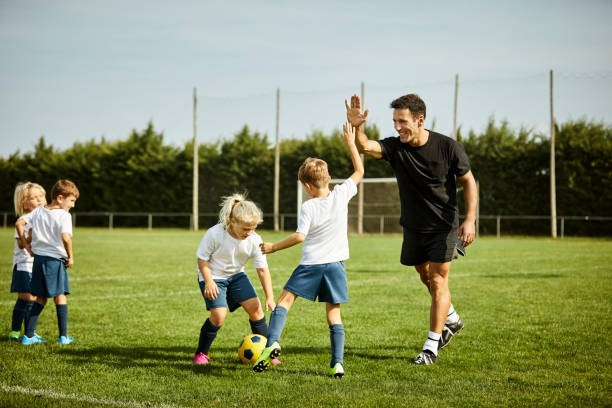Soccer coach high-fiving with boy during practice Smiling male soccer coach high-fiving with boy. Children are practicing on field. They are in sports uniforms. coach stock pictures, royalty-free photos & images