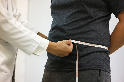 Doctor uses a tape measure to measure the waist of fat man Slimming Institute.