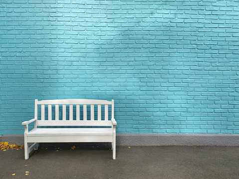 Single white wooden bench on a background of blue brick wall. The facade of the building painted in blue. Vintage photo with copy space.