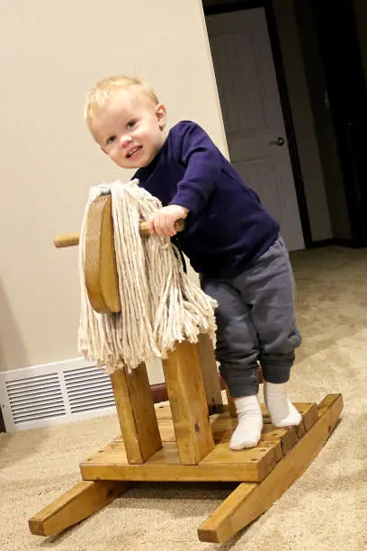 Young toddler boy child on wooden rocking horse with mop mane