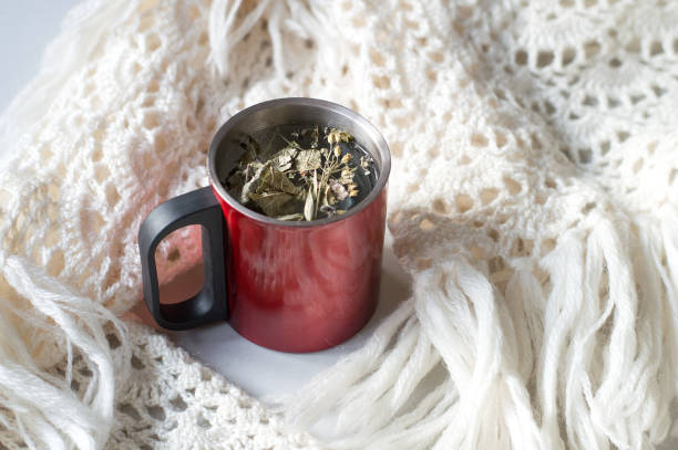 A cup of herbal tea in warmth containing red cup next to crocheted warm kerchief. Cold weather concept. Christmas time. Selective focus