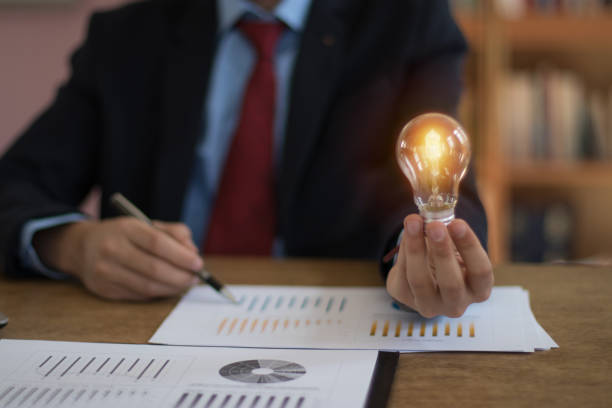 rachunkowość biznesowa z ręcznym trzymaniem żarówki koncepcji tło finansowe - light bulb led evolution development zdjęcia i obrazy z banku zdjęć