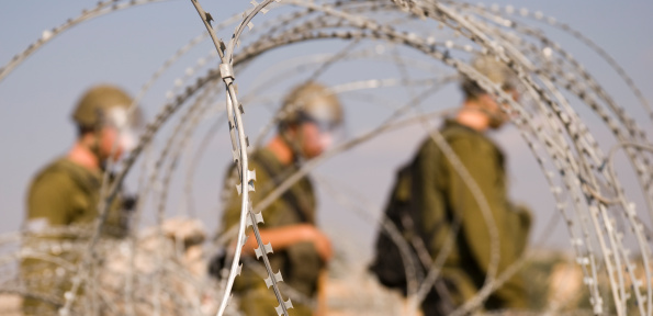 Three Israeli soldiers walk near razor wire near the Palestinian village of Bil'in in the West Bank.