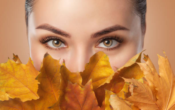 긴 속눈썹과 아름다운 스모키 눈 메이크업과 아름다운 여자는 얼굴 근처에 노란색 잎을 보유하고있습니다. 눈을 감습니다. 카메라를 보고 - leaf lookers 뉴스 사진 이미지