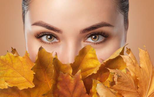 Beautiful woman with long eyelashes and with beautiful smokey eyes makeup holds yellow leaves near the face. Eyes close up. Looking at the camera