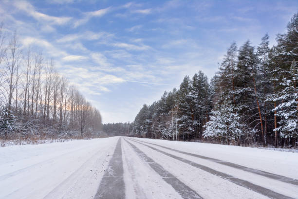 Patterns on the winter highway in the form of four straight lines. Snowy road on the background of forest. Winter landscape. stock photo
