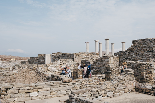 Delos, Greece - September 20, 2019: People walking amongst and take pictures of the ruins on island of Delos, an archaeological site in Greece near Mykonos in the Aegean Sea Cyclades archipelago.