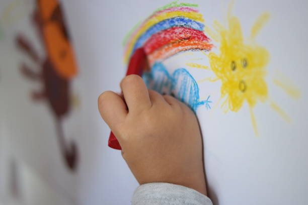 istock A child is drawing rainbow, cloud and sun on the wall in a pre school. 1180666964