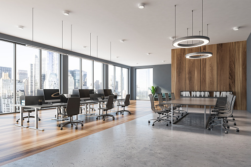 Corner of modern office with gray and wooden walls, open space area with gray computer tables and conference room with metal chairs. 3d rendering