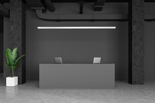 Interior of minimalistic industrial style office with gray walls, columns, concrete floor and simple grey reception desk with laptops on it. 3d rendering