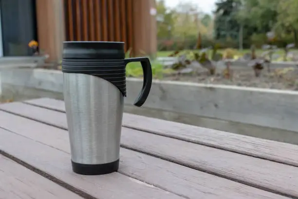 Metal thermo cup with hot drink, tea or coffee on the bench in park copy space, coffee on the go concept.