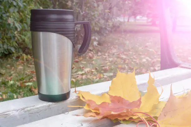 Season, autumn hot drinks and picnic concept - metal thermo coffee cup surrounded by colorful yellow leaves with copy space.