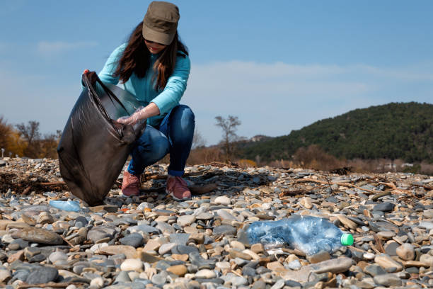voluntário mulher ajuda a limpar a praia de lixo plástico. dia da terra e conceito da melhoria ambiental. costa de pedra no fundo - mulher catando lixo - fotografias e filmes do acervo