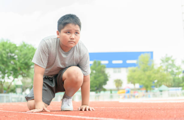 boy in starting position ready for running. fit and confident boy in starting position ready for running. kid athlete about to start a sprint looking forword. exercise concept overweight child stock pictures, royalty-free photos & images