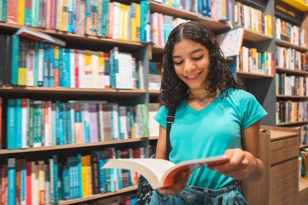 adolescente ragazza che legge libro in biblioteca - educazione secondaria di scuola media foto e immagini stock