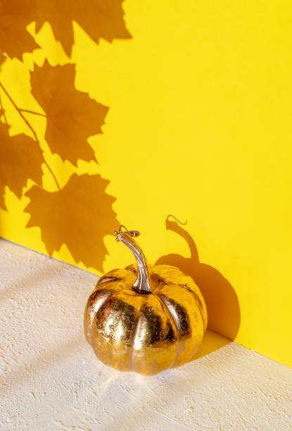 istock Golden pumpkin with a shadow from maple leaves on a yellow background. 1180710538