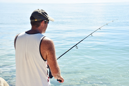 A Mid Adult Male on a Fishing Trip off Coastal Rocks in summer.