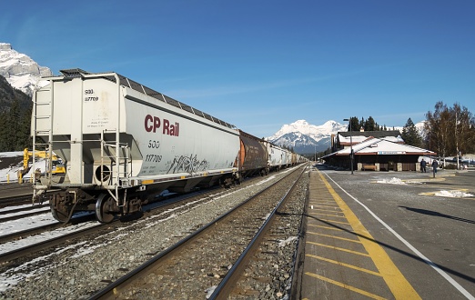 Banff, Alberta, Canada - October 11, 2019:  CP Rail Freight Train Cars at Railway Station with Distant Snowcapped Mountain Peaks of Banff National Park on the Horizon