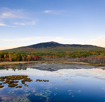 Drone view of the iconic New Hampshire mountain over Perkins Pond. Taken during fall season with peak foliage. Reflection of the mountain is visible on the pond’s surface.