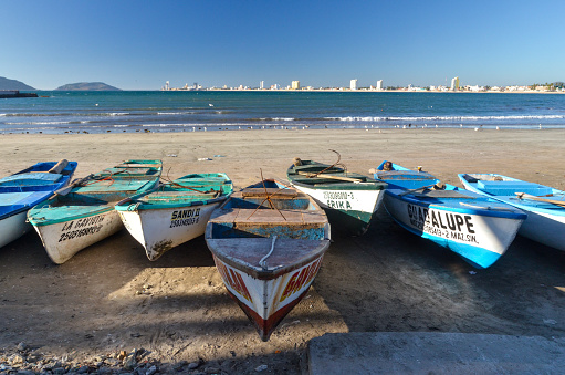 A wide angle of various fishing boats docked on a sandy beach with the tourism district across the bay