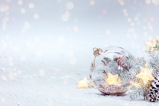 winter snowy white background with fir tree branch, glass ball and glowing lights garland