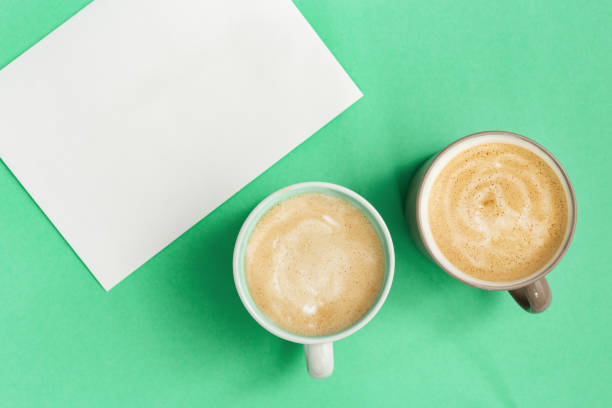 fermez-vous vers le haut de deux tasses de café cappuccino et papier blanc pour écrire des idées. temps de détente et de réflexion. la vue supérieure et plat se sont couchés avec le fond de menthe de couleur tred. - snack coffee instant coffee cappuccino photos et images de collection