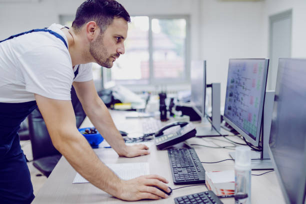 opinião lateral o trabalhador caucasiano sério da planta que usa o computador no quarto de controle. - setup operator - fotografias e filmes do acervo