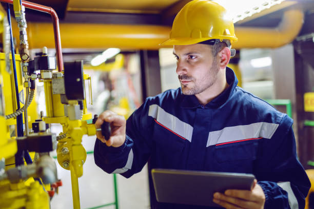 serio operaio dedicato all'impianto in abiti da lavoro e con casco protettivo sulla valvola di avvitamento della testa e tablet di tenuta. - technology engineer occupation heat foto e immagini stock