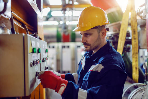 vue de côté du travailleur caucasien d'usine d'énergie dans des vêtements de travail et avec le casque sur la tête tournant sur l'interrupteur. - générateur dénergie photos et images de collection