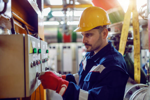Side view of caucasian energy plant worker in working clothes and with helmet on head turning on switch. Side view of caucasian energy plant worker in working clothes and with helmet on head turning on switch. generator stock pictures, royalty-free photos & images
