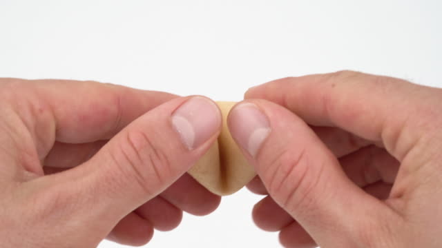 Close-up of male hands opening a fortune cookie with a card inside. Isolated, on white background.