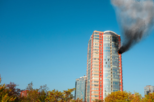 Skyscraper fire accident. Concept of firefighting problems at the height. Thick smoke billows from a window of apartment or office at high level