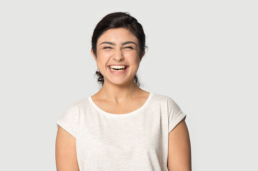Excited indian young woman in casual weat t-shirt posing isolated on grey studio background laughing, headshot portrait of overjoyed ethnic millennial girl feel happy pleased, humor concept