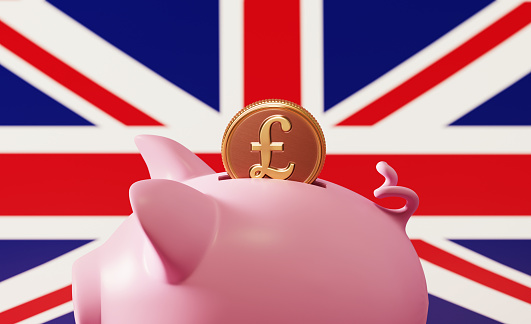 Piggy bank and pound coin over British flag background. Horizontal composition with copy space. Great use for savings concepts.