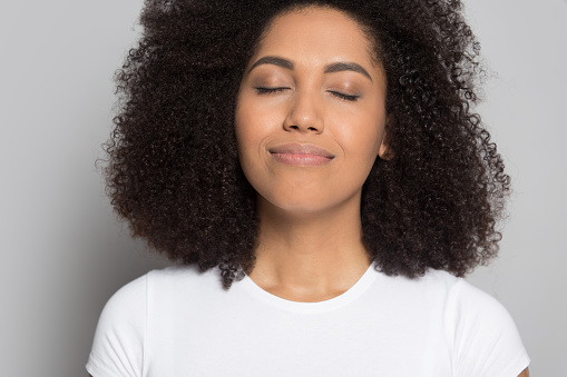 Close up of happy peaceful african American young woman isolated on grey studio background breathe fresh air, smiling calm biracial millennial girl relax relieve negative emotions, stress free concept