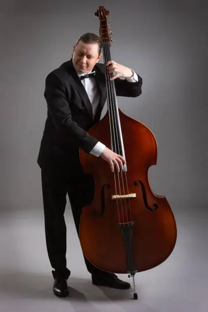 Photo of A man with a double bass on a gray background.