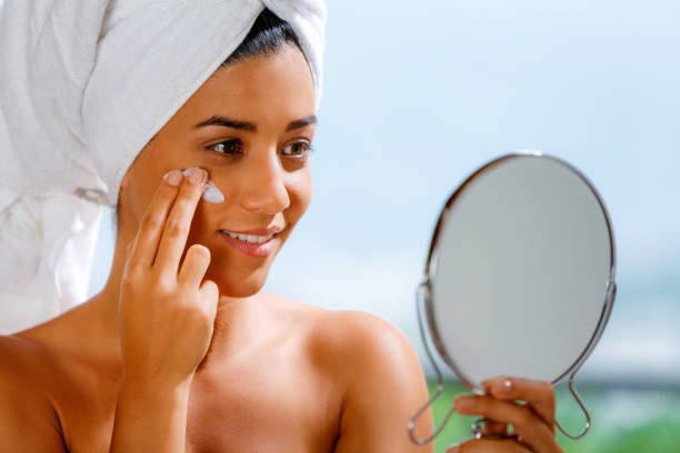 istock Cute and happy Hispanic young woman applying moisturizing cream using face mirror 1180755607