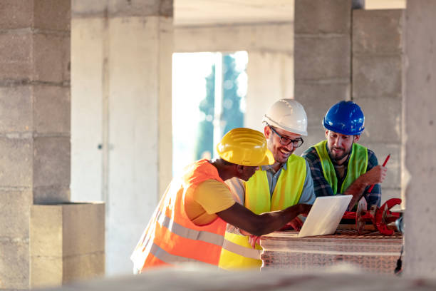 Male engineer directing his team Team of Multi-Ethnic construction workers wearing protective helmets and vests discussing project details with executive supervisor standing with tools and laptop. foreperson photos stock pictures, royalty-free photos & images