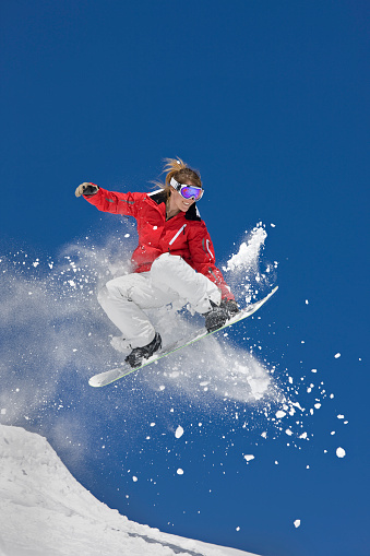 Female making snowboard jump in powder snow against clear blue sky.