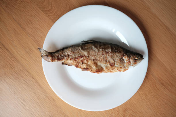 Fried fish on white plate on wooden surface, view from above