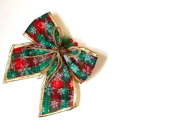 Beautiful bow on green-and-red ribbon with golden edges on white background. On the ribbon are patterns of snowflakes. Artificial coniferous twig on the bow. Copy space for your text.
