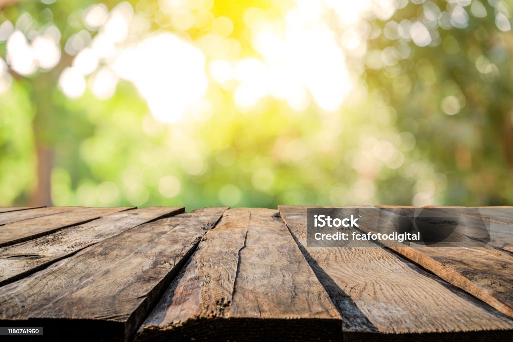 Backgrounds: Empty wooden table with defocused yellowish lush foliage at background Empty rustic wooden table with defocused yellowish lush foliage at background. Ideal for product display on top of the table. Predominant color are green and brown. XXXL 42Mp outdoors photo taken with SONY A7rII and Zeiss Batis 40mm F2.0 CF Table Stock Photo