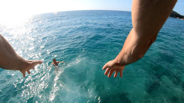 POV behind man's arms as he jumps off cliffs over sea