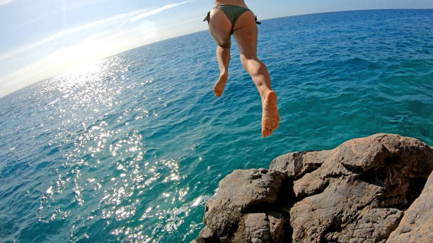 istock Young woman jumps off cliffs over sea 1180766373