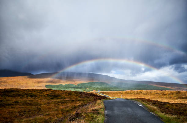 A double rainbow over the landscape in scotland along the route of the north coast 500. The road leads through the landscape.
