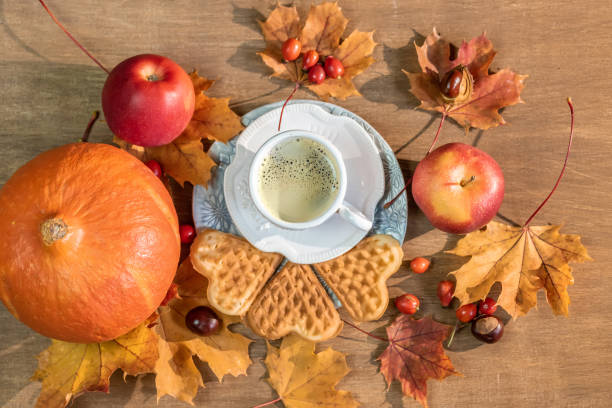 Autumn, fall leaves, a hot steaming cup of coffee, pumpkin and a warm sweater on a wooden table background.