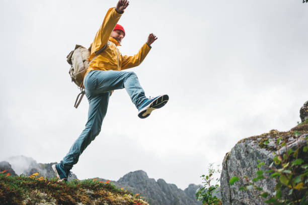 adventure tourist jumping on rocks over cliff. brave man traveler hiking trail in authentic wilderness - rock norway courage mountain imagens e fotografias de stock